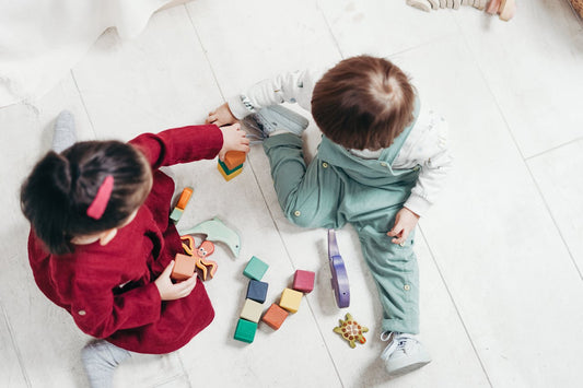 Twee kinderen spelen op de vloer met houten blokken