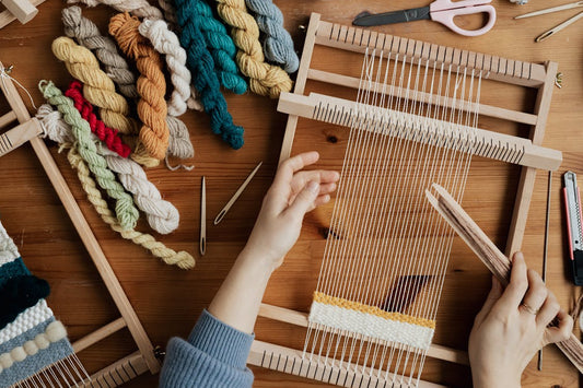 Handen weven op een houten weefraam met bollen wol ernaast